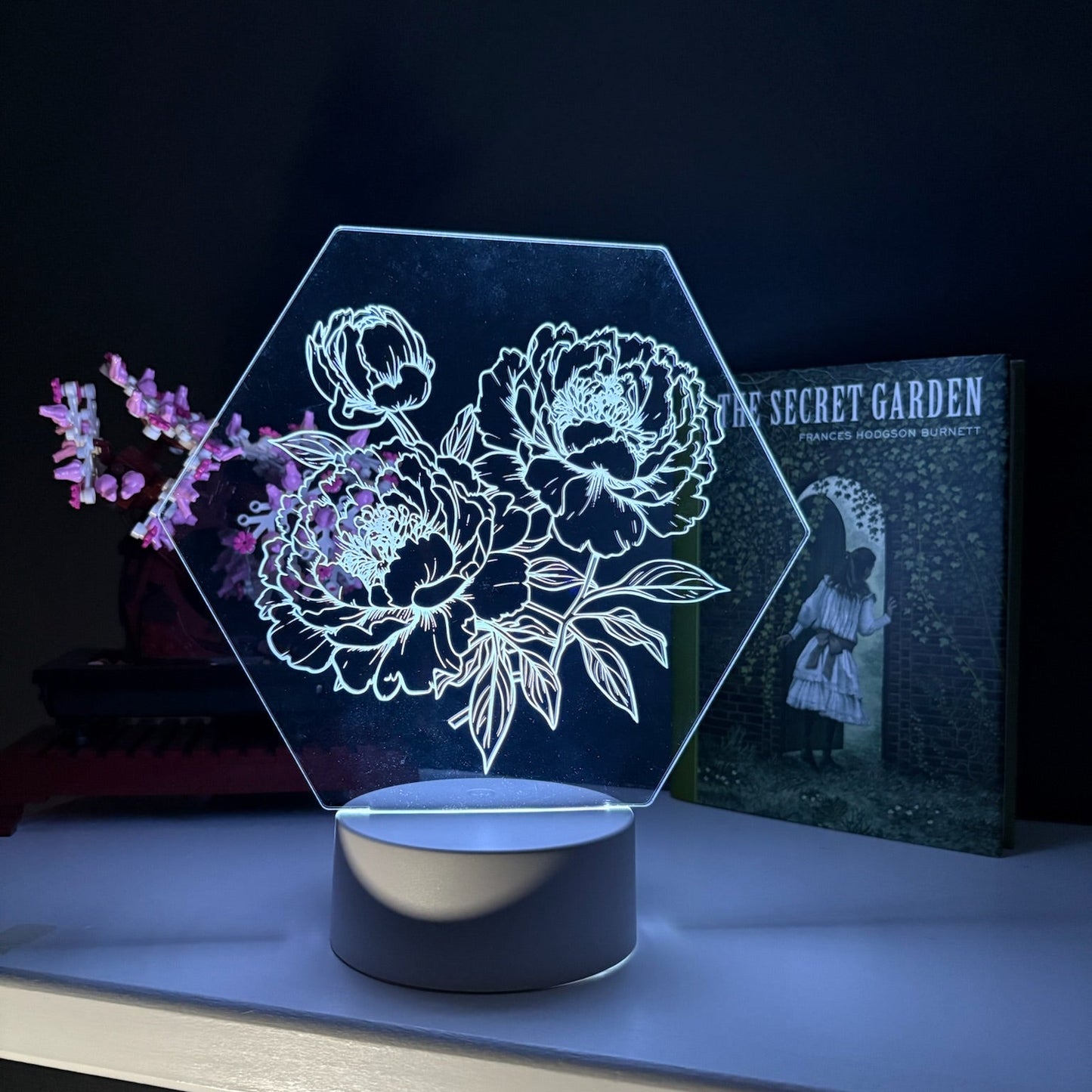 Hexagonal floral LED lamp on a dark surface with a book in the background