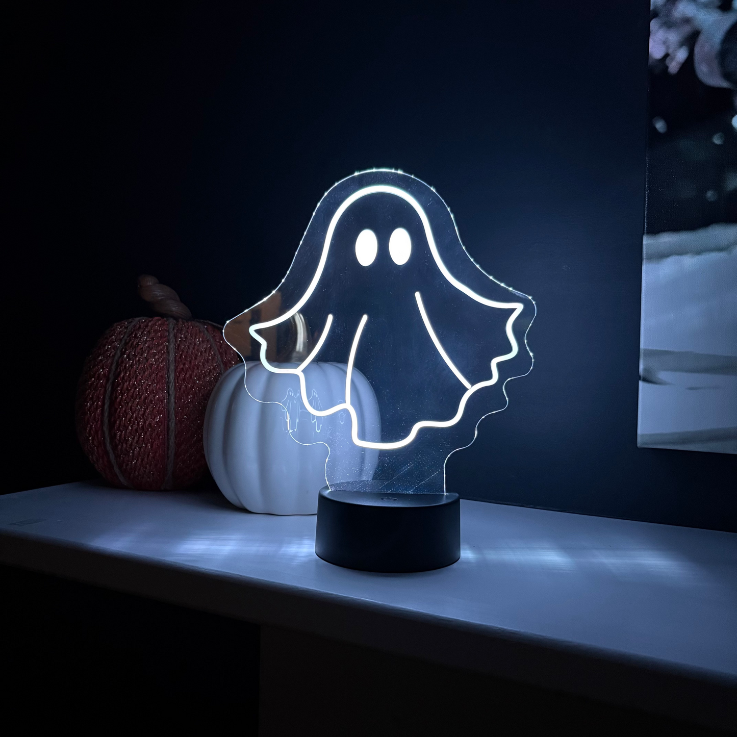 Ghost-shaped night light on a dark background with pumpkins