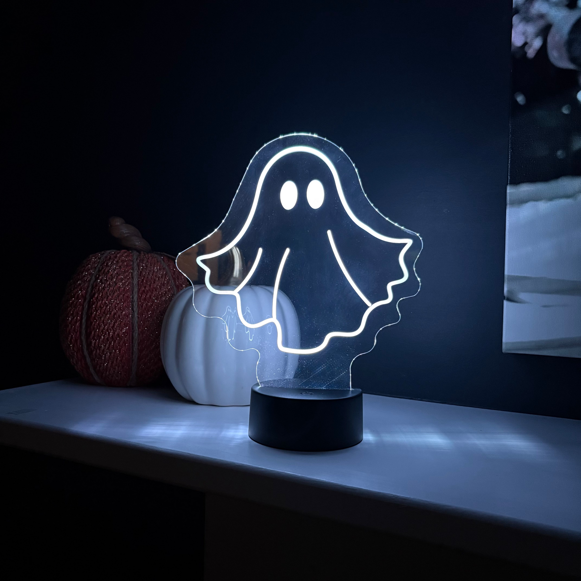Ghost-shaped night light on a dark background with pumpkins