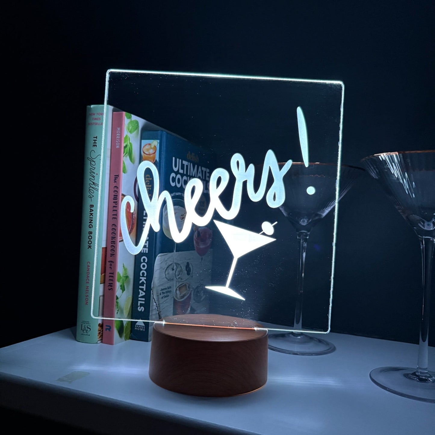 LED sign with 'Cheers!' text on a table with books and glasses in the background
